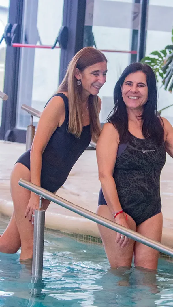 Dos mujeres sonríen al entrar a una piscina termal cubierta